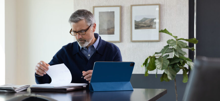 A man sits at a desk with a notepad and a tablet.