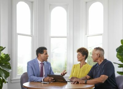 Two men and a woman talk at table with a tablet