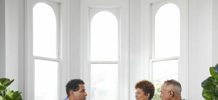 Two men and a woman talk at table with a tablet