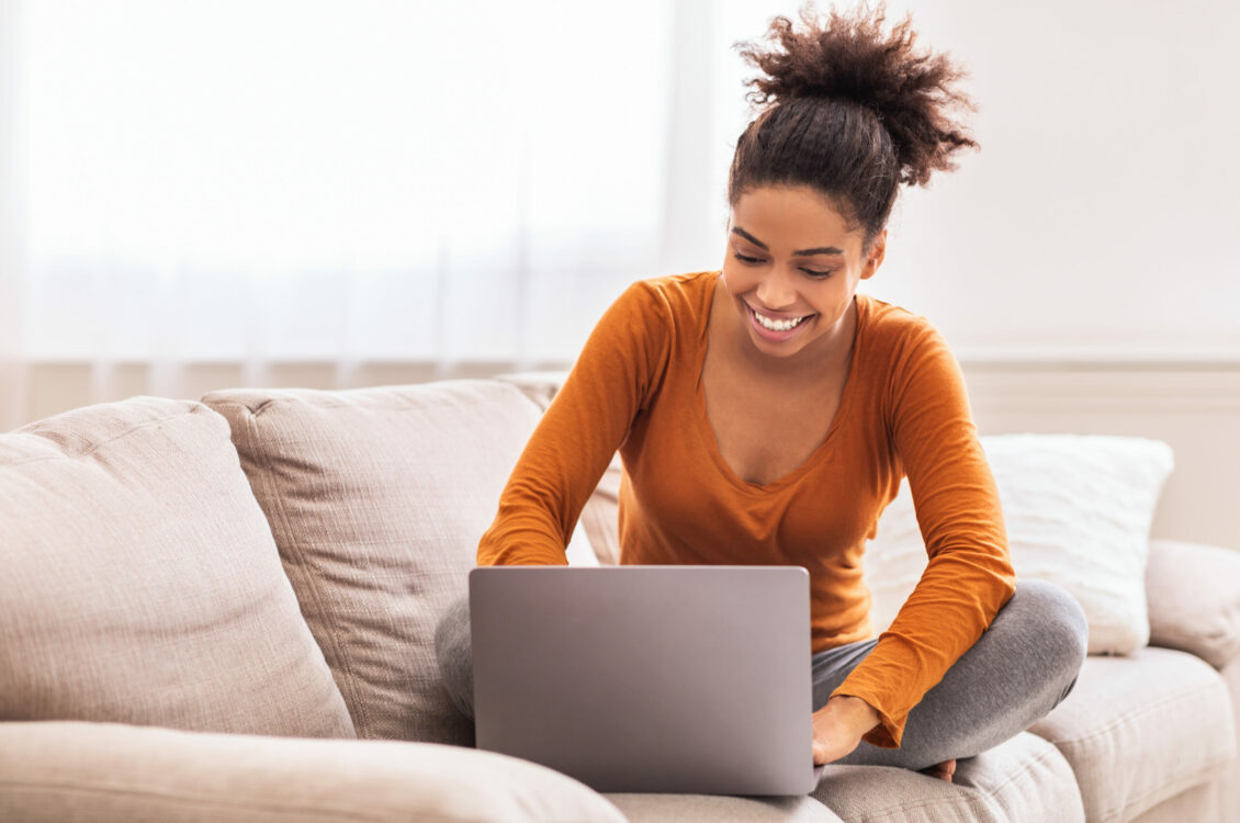 Happy African American Lady Freelancer Using Laptop Working Online From Home Sitting On Sofa Indoor. Copy Space, Selective Focus