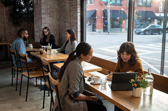 Two women talk over a computer at a coffee shop.