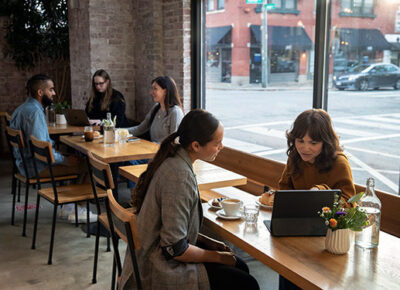 Two women talk over a computer at a coffee shop.