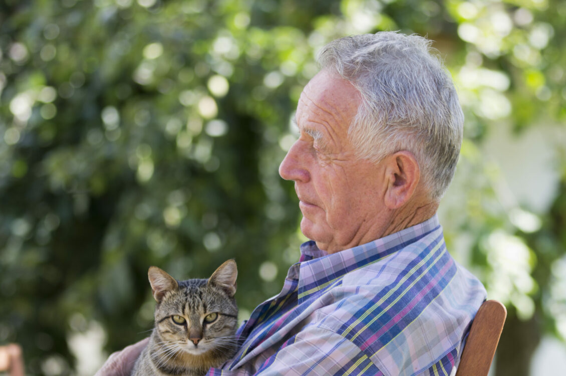 A senior man cuddles his cat outside.