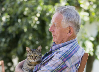 A senior man cuddles his cat outside.