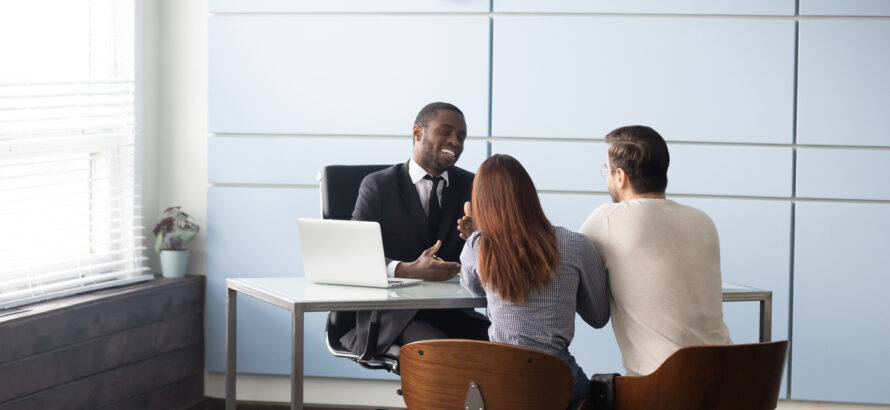 Happy smiling african american male realtor broker banker talking consulting young married couple. Full length millennial family spouse meeting real estate agent or financial advisor at office.