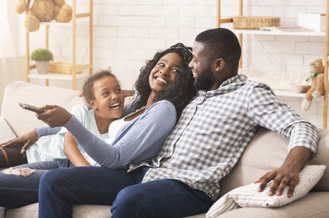 Joyful black family having fun together, relaxing on sofa at home.