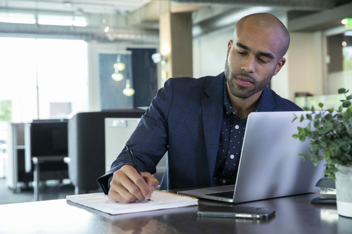 A professional taking notes and working with a laptop