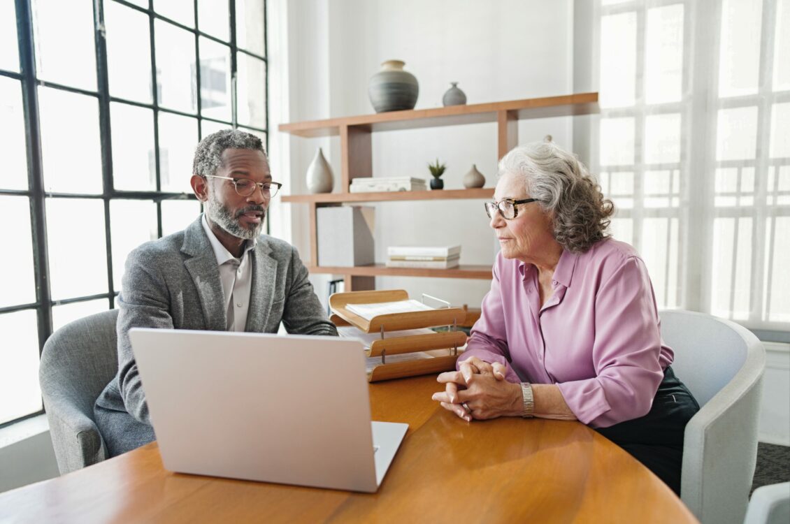 A professional showing information on a laptop to another professional while having a discussion.