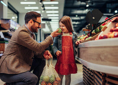 A guardian holding up a fruit to a little girl to smell at the supermarket.