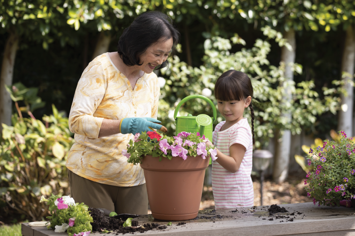 A child helping an elderly woman with watering the plant.