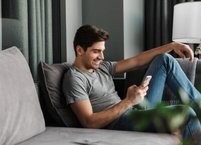 A guy relaxing on a sofa while checking out their phone.