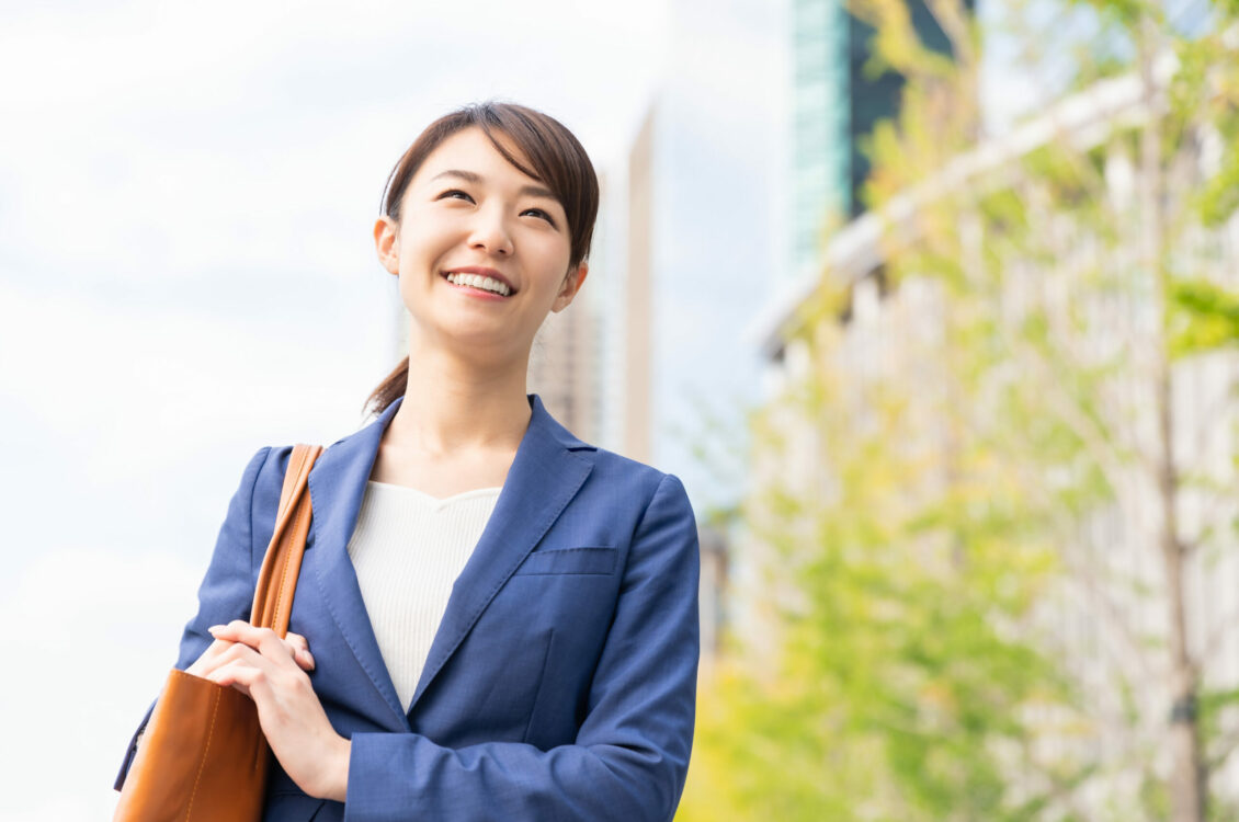 A woman standing outside, smiling while looking into the air.