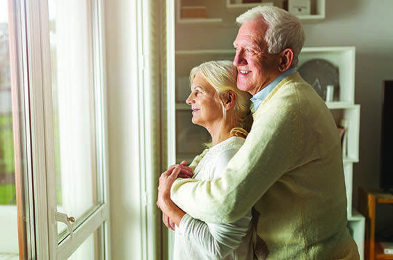 An elderly couple embraces as they look out of a window.