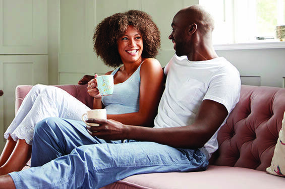 A young, smiling couple drinks coffee on a couch.
