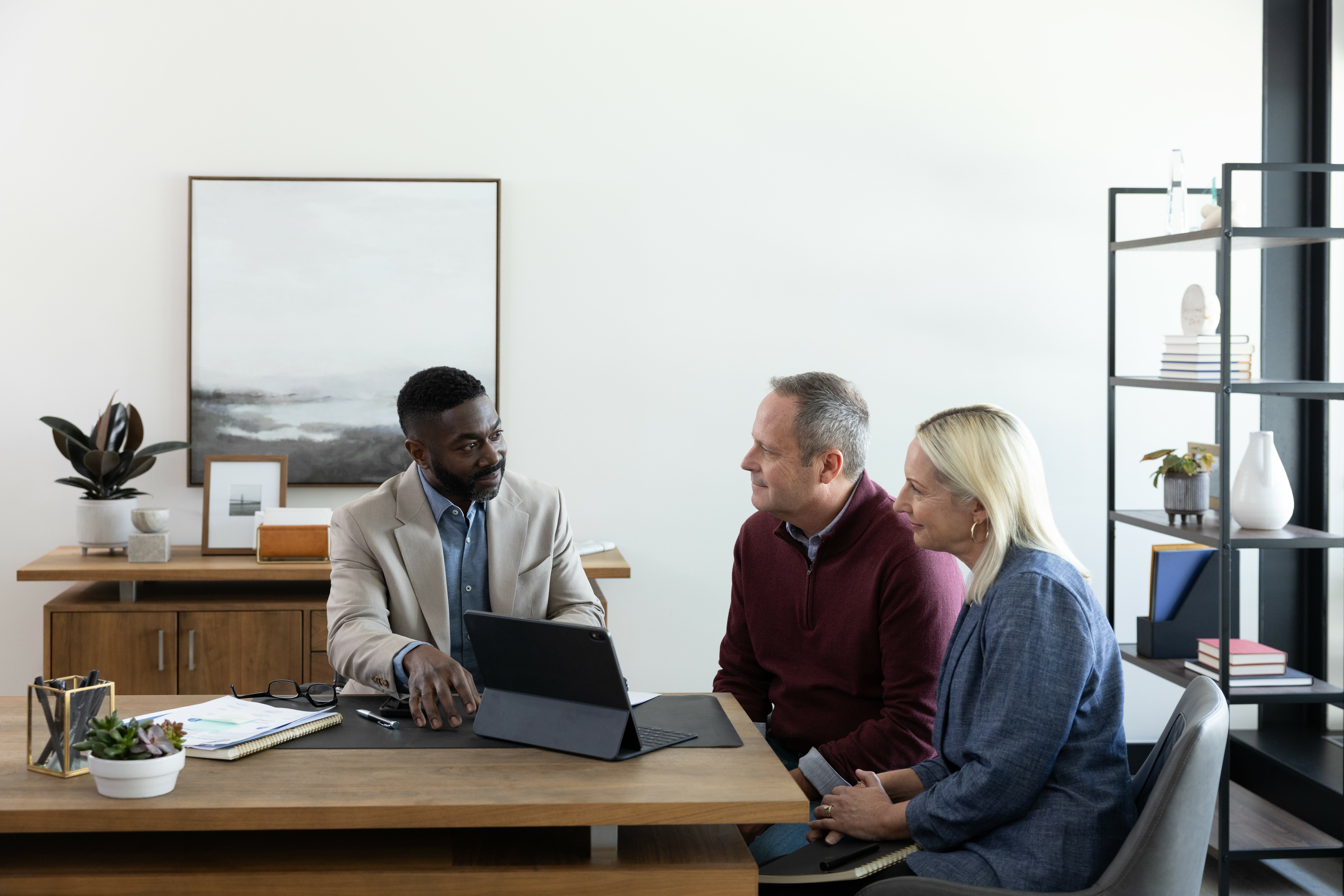 A couple speaking to a man presenting on a tablet in an office.