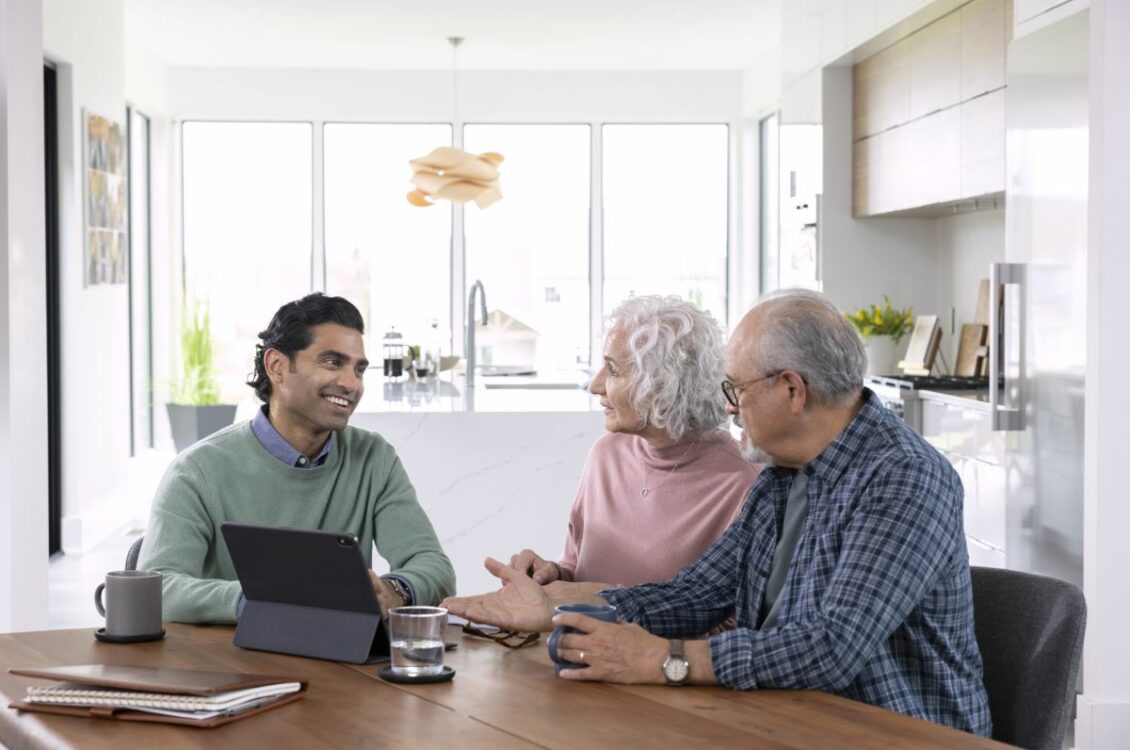 A smiling man shows an elderly couple something on a tablet.